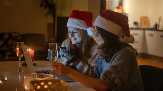 Two Women Talking On A Laptop In Christmas Hats In Their Home