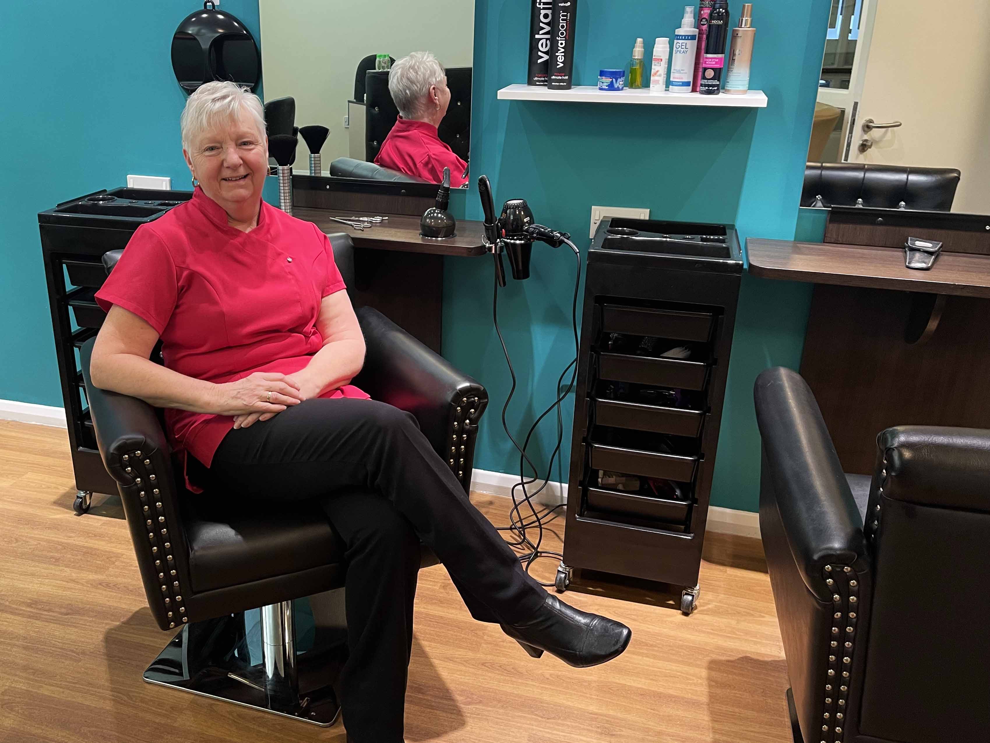 Village hairdresser sat in a hairdressers chair smiling