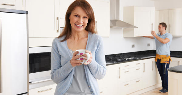 Woman In Kitchen While Handyman Checks Cupboards