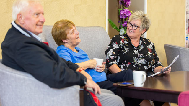 An older couple sat down talking to a member of staff over a cup of coffee